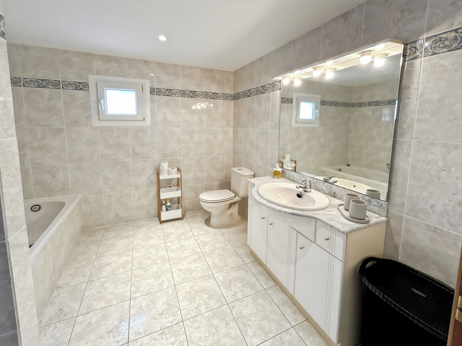 Une salle de bain équipée d’une baignoire, de toilettes, d’un lavabo et d’un grand miroir avec éclairage.