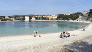 A beach with clear water, people sunbathing, and buildings in the background.