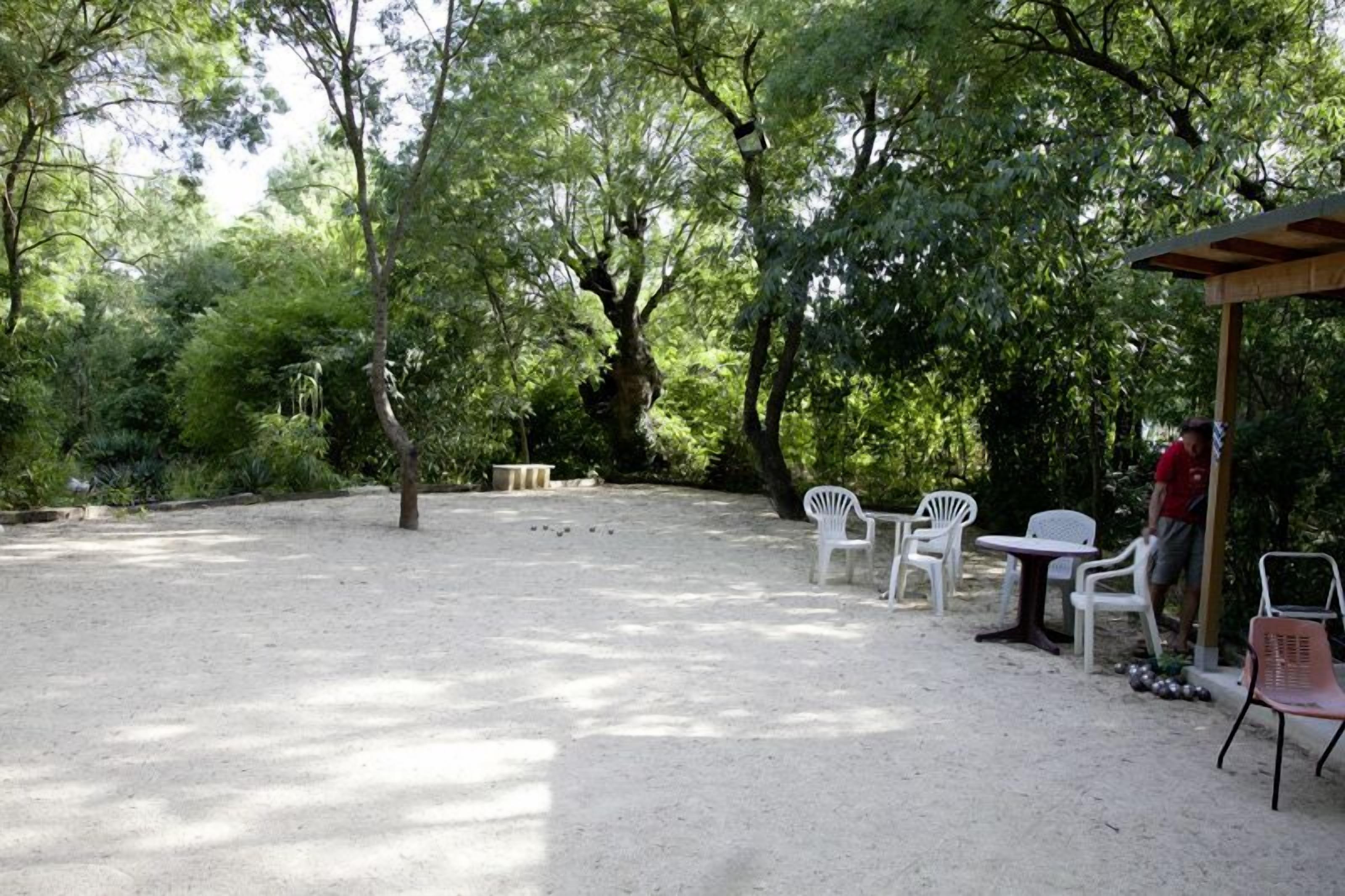 Un espace extérieur aménagé avec des chaises et des tables en plastique blanc, entouré d’arbres et de verdure.