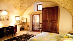 Una habitación acogedora con techo de piedra, una cama con colcha estampada, un escritorio con sillas y un armario de madera.