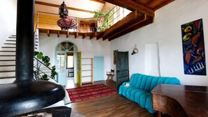 Un salón amplio con techo alto, vigas de madera, un sofá azul a rayas, una estufa negra y un cuadro en la pared.