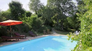 Una piscina con sillas de descanso y una sombrilla, rodeada de exuberante vegetación.