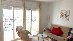 A living room with a sofa, a rocking chair, a small table, and a view through large windows. - APARTAMENTOS AQUARIUM (REF 31). NEXT TO THE BEACH. RENOVATED. (Roses)
