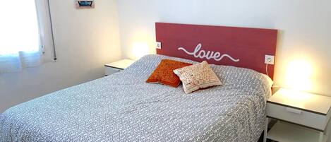 A neatly made bed with patterned bedding, two pillows, a headboard with 'love' written on it, bedside lamps, and a small nightstand.