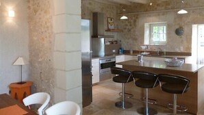 Una cuina moderna amb una illa central, tamborets i una zona de menjador amb caires.