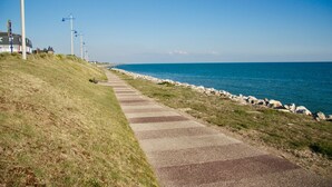 A coastal walkway with a paved path, grassy areas, and a rocky shoreline.