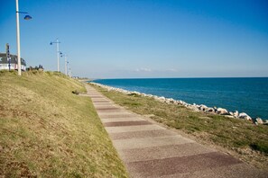 A coastal walkway with a paved path, grassy areas, and a rocky shoreline.