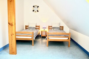 Une chambre à coucher avec deux lits en bois, une table de chevet, une lampe et un panneau d’accueil accroché au mur.