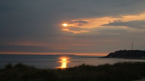 A sunset over a coastal landscape with a lighthouse on a hill.