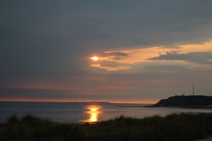 A sunset over a coastal landscape with a lighthouse on a hill.