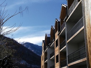 A multi-story building with balconies, set against a mountainous backdrop.