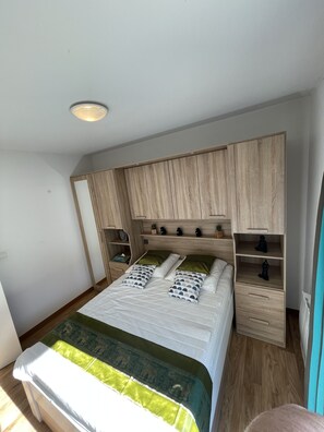 Une chambre à coucher comprenant un lit, une tête de lit en bois, des tables de chevet et une armoire intégrée.