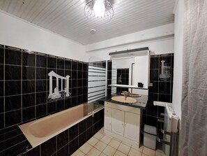 A modern bathroom with black and white tiles, a freestanding bathtub, a sink with a mirror, and a shower area. - Gîte “Les Tamaris” (Saint-Pierre-De-Buzet)