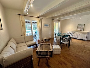 Ein Wohnzimmer mit Sofa, einem Glastisch, einem Esstisch mit Stühlen und einer Küchenzeile mit Schrank.