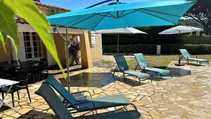 An outdoor patio with stone flooring, a table with chairs, and several lounge chairs under umbrellas. - Family home with private pool, fenced garden, 500 meters from the beach. (La Croix-Valmer)