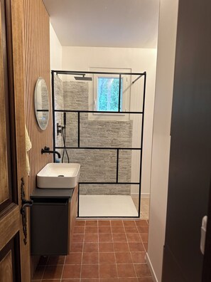 A bathroom with a stone-textured wall, a window with a view of trees, a mirror, and a sink. - Family home with private pool, fenced garden, 500 meters from the beach. (La Croix-Valmer)