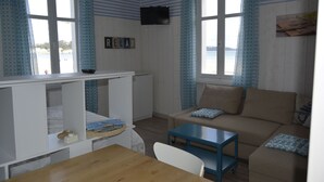 Une pièce avec une table en bois, un canapé, un téléviseur fixé au mur et une fenêtre donnant sur la plage.