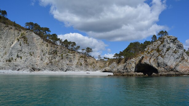 Un paysage côtier caractérisé par des falaises rocheuses, une plage et un ciel bleu dégagé.