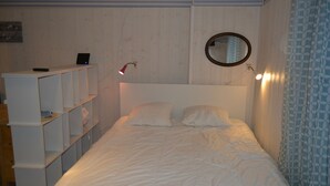 Un lit bien fait, avec une tête de lit, une table de chevet avec une lampe et une étagère contenant des livres et une télécommande.