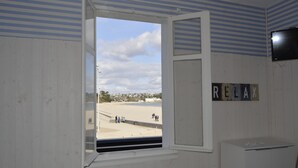 Une chambre avec une fenêtre donnant sur la plage, une pancarte indiquant « DÉTENTE » et un téléviseur fixé au mur.