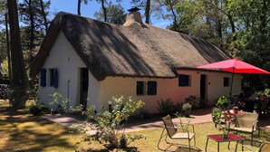 Ein rustikales Haus mit Strohdach, einem kleinen Garten und Sitzgelegenheiten im Freien.