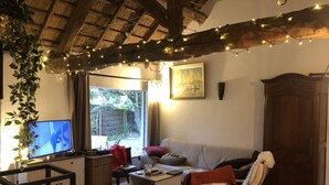 Ein gemütliches Wohnzimmer mit Fernseher, einer Couch, einem Holzstuhl, einem kleinen Tisch und einer Pflanze.