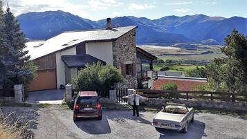 Un edificio de piedra de dos pisos con un cocheras, un automóvil descapotable estacionado y una persona parada adelante.