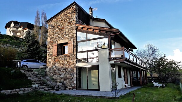 Ein zweigeschossiges Steinhaus mit Balkon, ein Auto auf der Auffahrt und ein Stuhl davor.