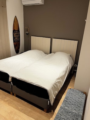 A bedroom with a bed, a surfboard on the wall, and a small rug.