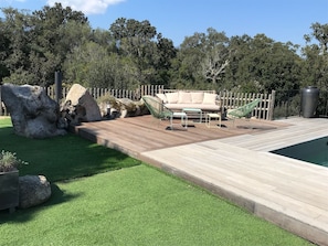 A wooden deck with a pool, a beige sofa, and a hammock. - Villa sotta-porto vecchio in the countryside heated pool (Sotta)
