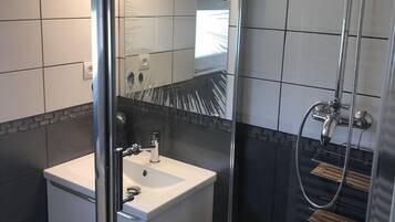 A modern bathroom with a glass-enclosed shower, a white sink, and a large mirror.