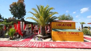 A beachside location with a wooden sign indicating 'PEDALOS' and 'PLANCHES'.