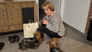 Une personne assise sur le sol, avec deux chiens, un meuble en bois, un vase et une porte en arrière-plan.