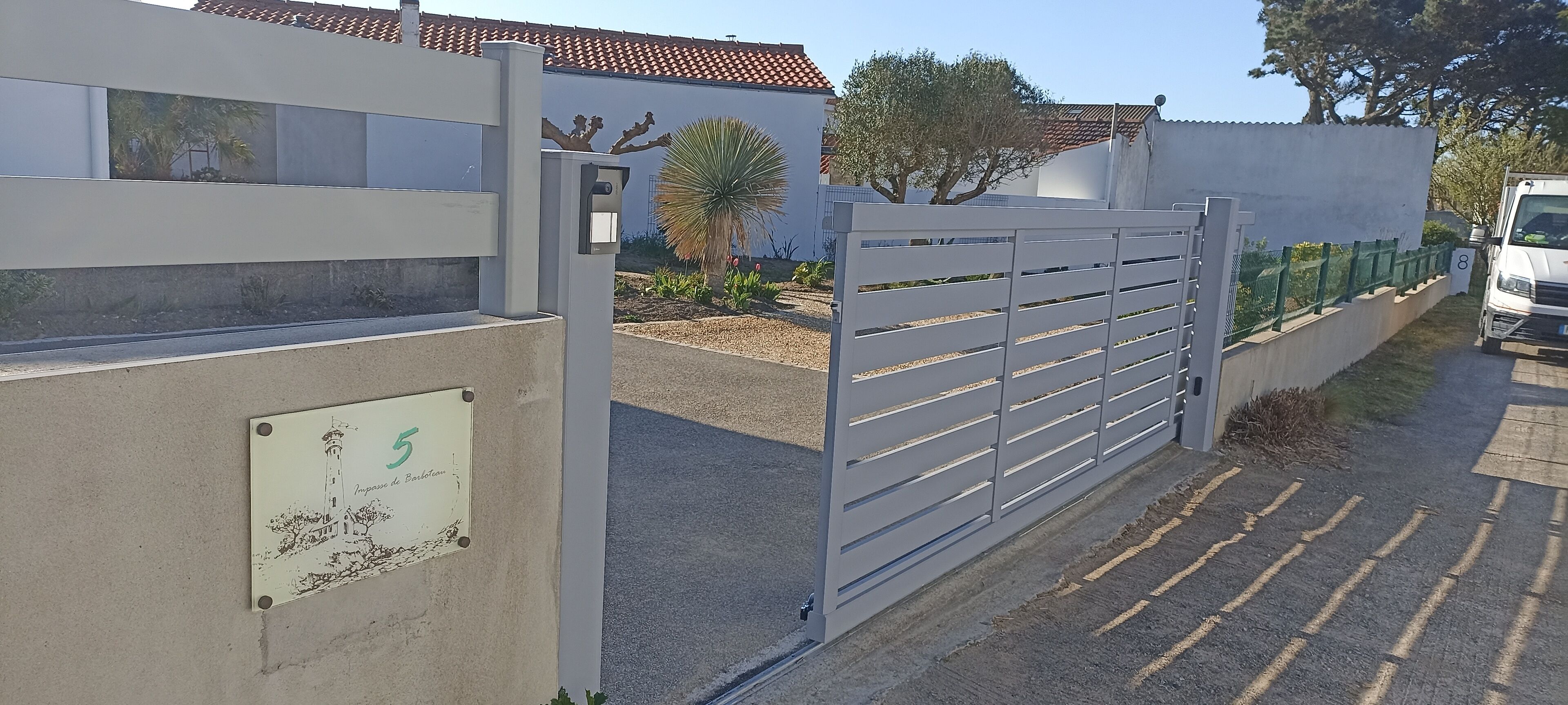 A gated entrance with a security camera, a numbered sign, and a vehicle parked nearby.