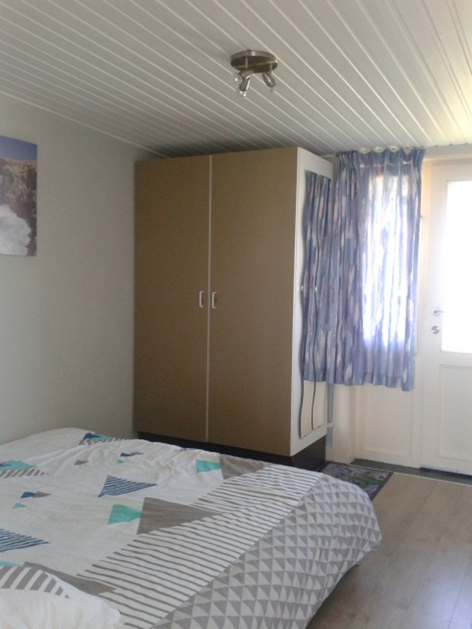 Ein Schlafzimmer mit einem Bett, einem Kleiderschrank, einer Tür mit Vorhängen und einer Deckenleuchte.