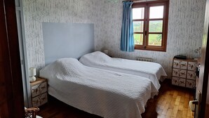 Une chambre avec deux lits, un plancher en bois, une fenêtre avec des rideaux bleus et un plafond en bois.