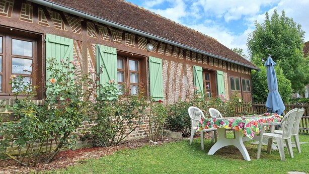 Un bâtiment traditionnel avec une façade en briques, des volets verts et un jardin agrémenté d’une table et de chaises.