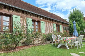 A traditional building with a brick facade, green shutters, and a garden area with a table and chairs.