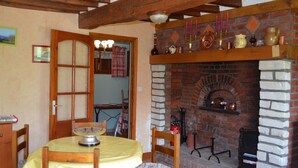 Un coin repas agrémenté d’une cheminée en briques, de poutres en bois et d’une table dressée pour deux personnes.