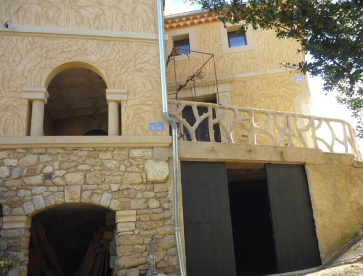 Un edifici amb façana de pedra, un balcó amb barana de ferro forjat i un gran portal d'arc.