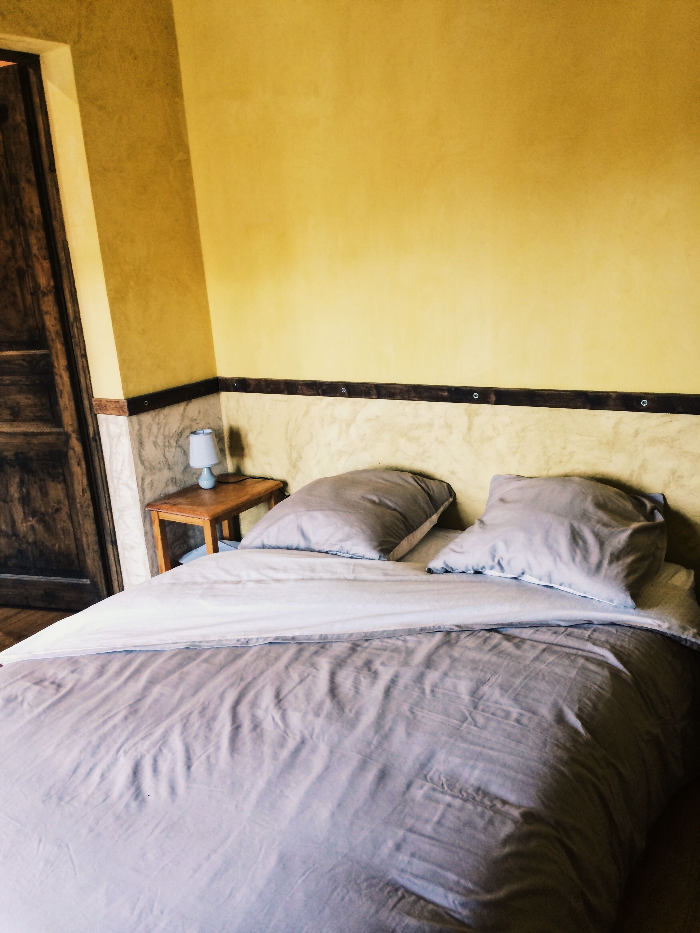 Una cama con cabecera, una mesita de noche con lámpara y una puerta de madera.