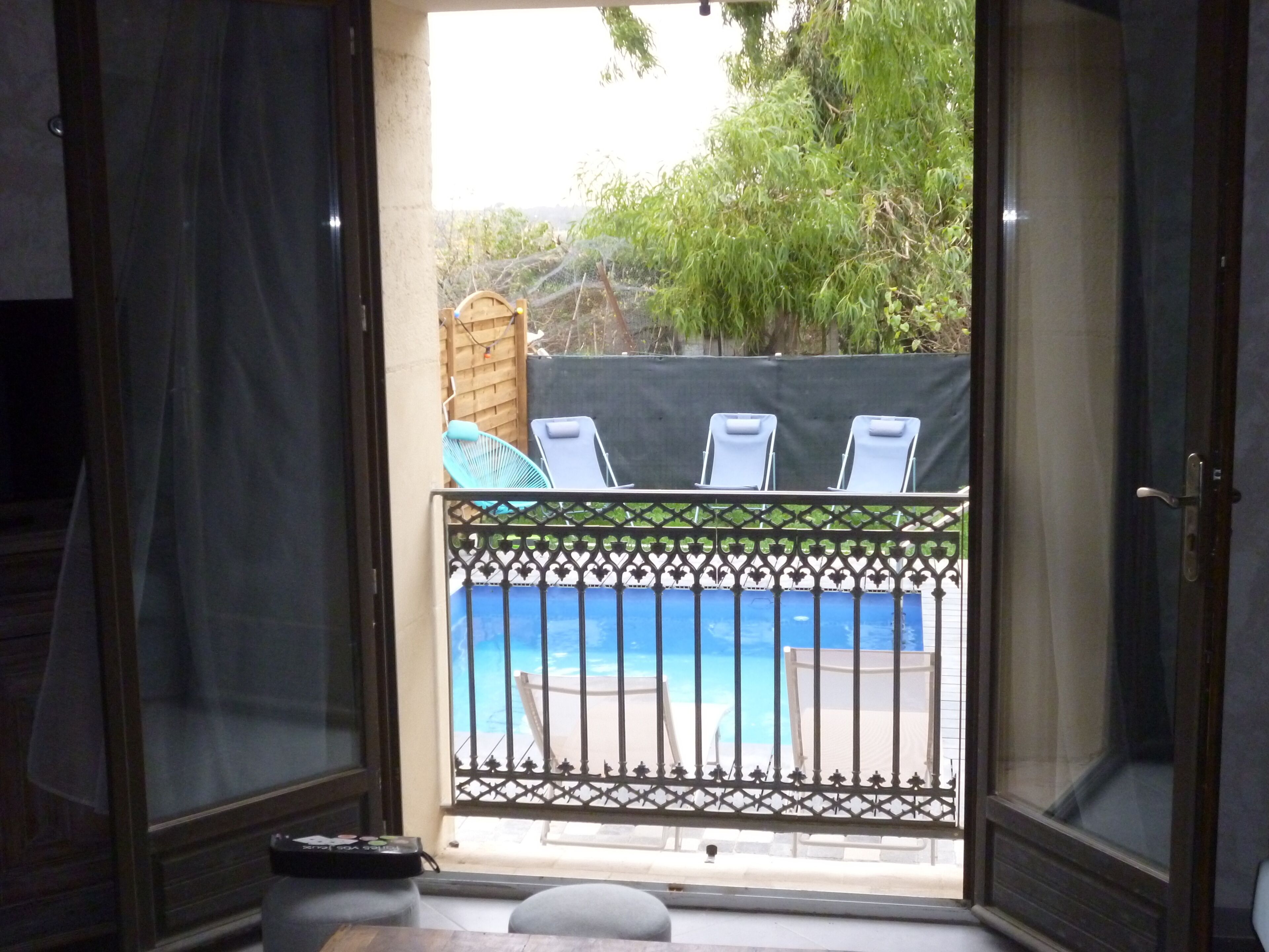 A balcony with a view of a swimming pool, a wooden fence, and two lounge chairs.
