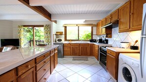 A kitchen with wooden cabinets, a washing machine, and a large window. - Villa Maharepa Beach by ENJOY VILLAS/3 bdrm with AC/2 bath/private pool + beach (Moorea-Maiao)