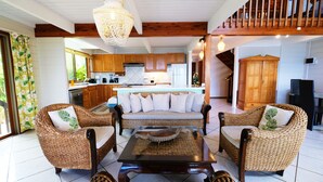 A spacious living area with wicker furniture, a central coffee table, and a kitchen in the background. - Villa Maharepa Beach by ENJOY VILLAS/3 bdrm with AC/2 bath/private pool + beach (Moorea-Maiao)
