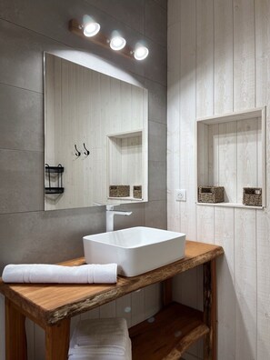 Un baño con tocador de madera, lavamanos blanco y un espejo grande con luces arriba.