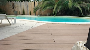 Een houten terras met een zwembad op de achtergrond.