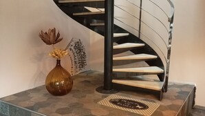 Een wenteltrap met een zwarte metalen leuning, een vaas met gedroogde bloemen en een decoratief vloerkleed op de landingsplaats.