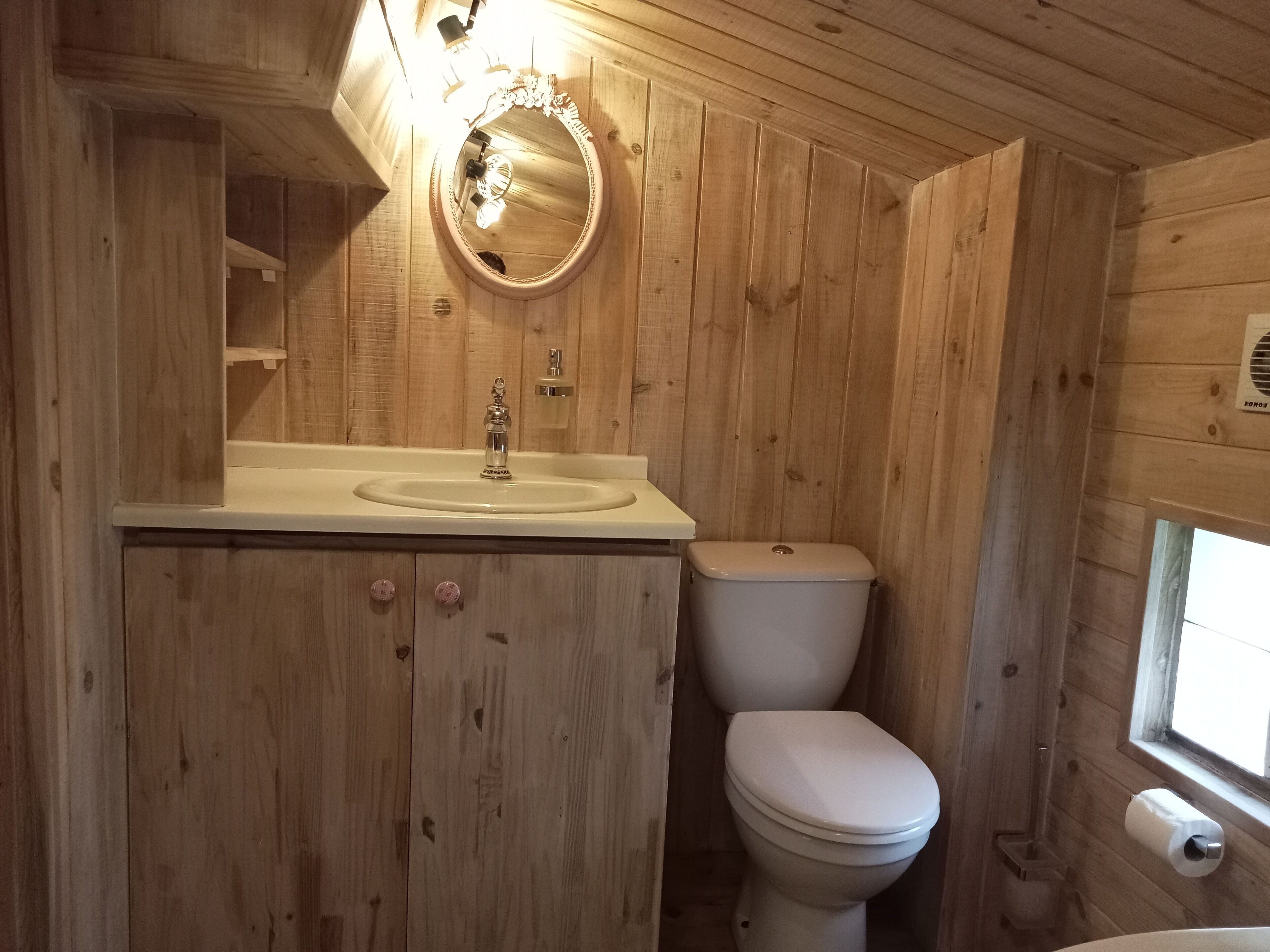 A wooden cabin bathroom with a sink, toilet, and a mirror above the sink.