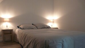 Een netjes opgemaakt bed met blauwe accenten, twee nachtkastjes met lampen en een houten vloer.