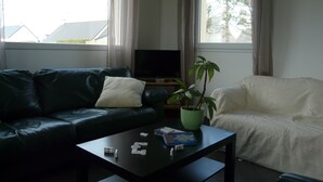 A living room with a green sofa, a white sofa, a coffee table with dominoes, a potted plant, and a television.